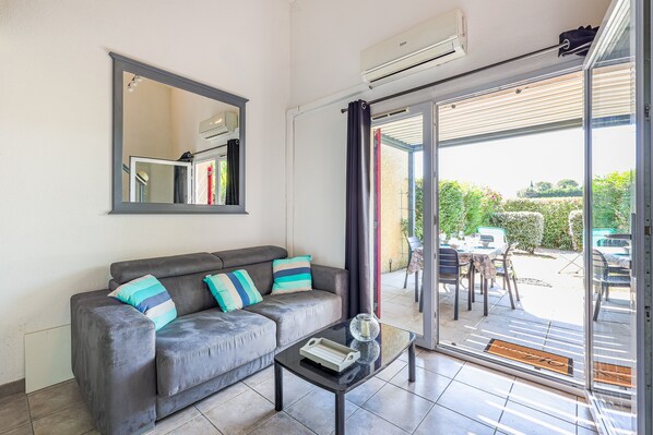 A modern living room with a grey sofa, a glass coffee table, and a large mirror.