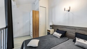 Ein modernes Schlafzimmer mit zwei Betten, einem Holzschrank, einem Nachttisch mit Lampe und einer Wandleuchte.