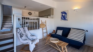 Een moderne woonkamer met een trap, een blauwe bank, een witte fauteuil en een houten salontafel.
