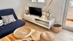 Een moderne woonkamer met een donkerblauwe bank, een witte televisiemeubel, een televisie en een groot raam met uitzicht op het landschap.