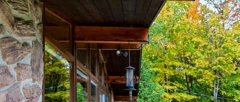 A wooden deck with a stone wall on one side and a glass door leading to a covered porch.
