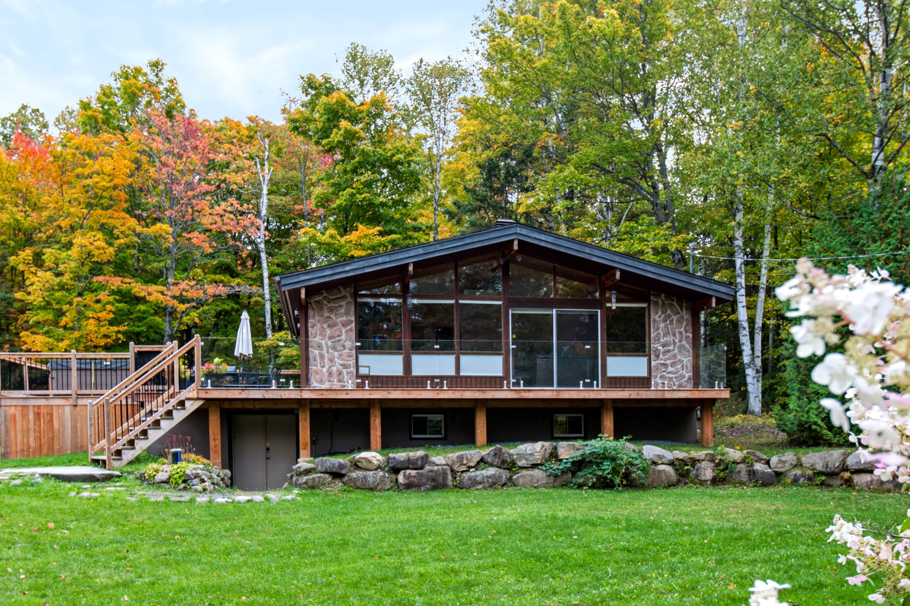 A modern cabin with a stone facade, large windows, and a wooden deck.