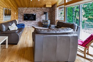 A cozy living room with a brick fireplace, leather sofas, and a television mounted on the wall.