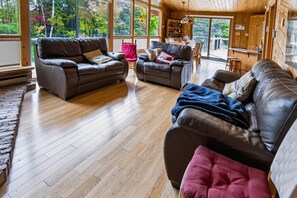 A spacious living room with a wooden floor, leather sofas, and a dining area with a table and chairs. - Le Coyote 5 acre private forest (Chertsey)