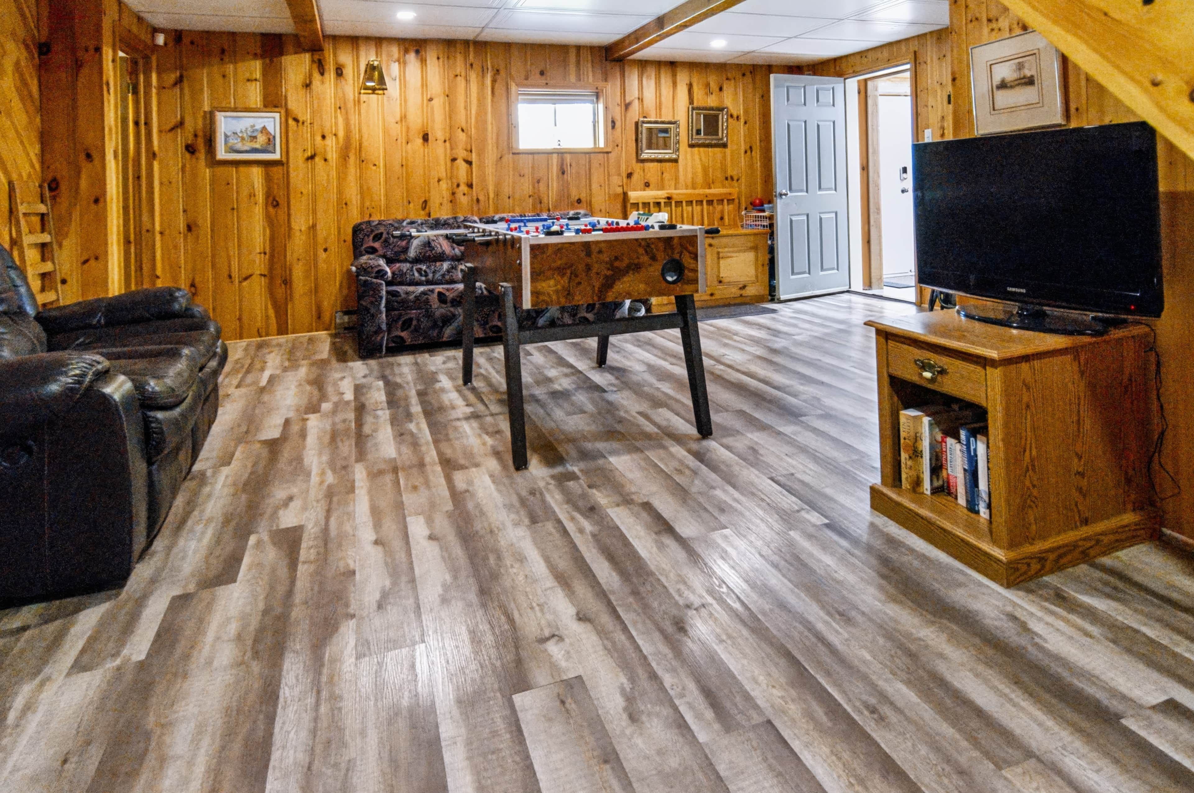 A cozy room with a foosball table, a sofa, a television, and a bookshelf.