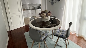 Een eetgedeelte met een ronde tafel, stoelen, een kroonluchter en een keuken op de achtergrond.