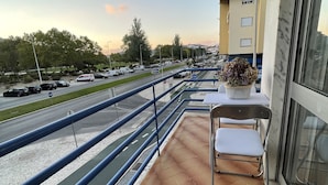Een balkon met uitzicht op een weg, een stoel en een plant in pot.
