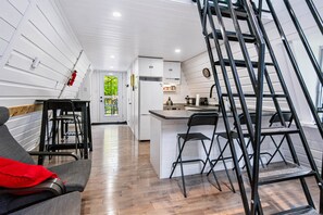 Cocina compacta con armarios blancos, una isla central y una escalera metálica negra.