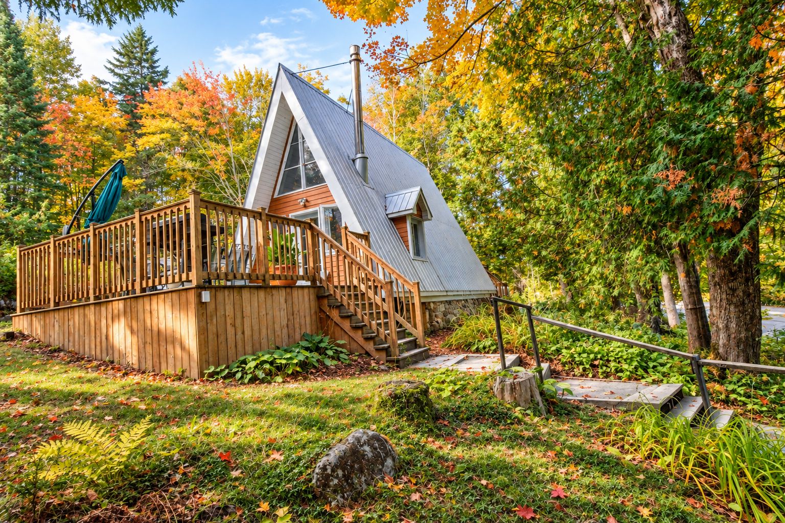 Une cabane dotée d’une terrasse en bois, d’un escalier et d’un toit en métal, entourée du feuillage automnal.