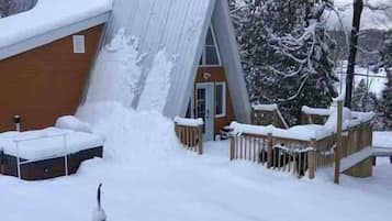 Un edificio cubierto de nieve con una terraza de madera y un techo de metal.