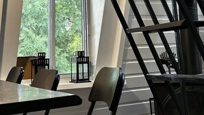 A modern interior with a staircase, large windows, and a dining area with tables and chairs.