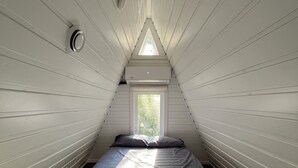 A small, sloped-roofed room with a single bed, a window, and a ceiling vent.