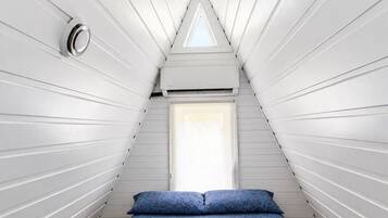 Una habitación con techo inclinado, cama con colcha estampada y ventana con vistas.