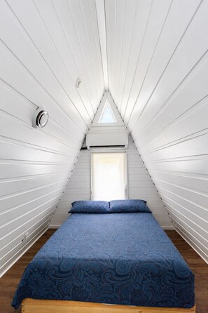 A room with a sloped ceiling, a bed with a patterned bedspread, and a window with a view. - Le Petit Lièvre CITQ 298679 (Chertsey)