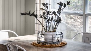 Une table à manger sur laquelle repose un panier en fil métallique contenant une plante en pot, le tout posé sur un set de table en fibres tressées.