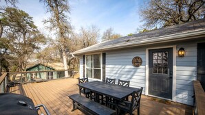 Une terrasse avec une table et des bancs en bois, un barbecue et un bâtiment doté d’une porte et de fenêtres.