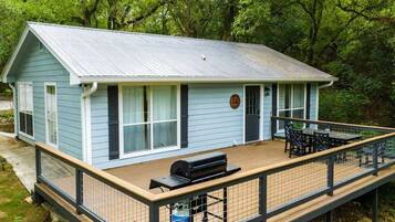 Enjoy a peaceful retreat in this cozy cabin surrounded by lush trees and greenery, featuring a front porch with a table and chairs, and a deck with a grill.