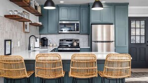 A kitchen with teal cabinets, a stainless steel refrigerator, a microwave, and a stove. There are wicker chairs at the island. - Pet-Friendly Cabin | Scenic River Views | Sleeps 5 (Kyle)