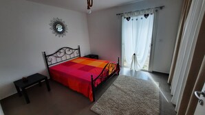 A bedroom with a bed, a nightstand, a wall-mounted mirror, and a window with curtains. - Maison au Calme (Aléria)