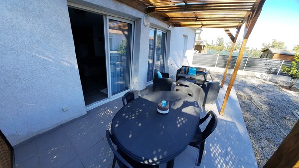 A covered patio with a round table and chairs, a sliding glass door, and outdoor furniture. - Maison au Calme (Aléria)