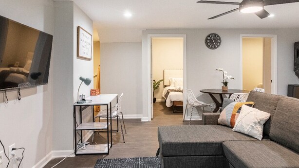 A modern living room with a gray sofa, a dining table with chairs, a ceiling fan, and a TV mounted on the wall. - 🔥 Spacious 3BR Basement APT near ATL Airport/ 10 Mins Downtown! Sleeps 8🔥 (East Point)