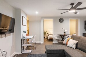 A modern living room with a gray sofa, a dining table with chairs, a ceiling fan, and a TV mounted on the wall. - 🔥 Spacious 3BR Basement APT near ATL Airport/ 10 Mins Downtown! Sleeps 8🔥 (East Point)