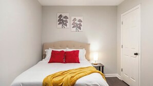 A hotel room with a bed, a nightstand, a lamp, and two wall art pieces. - 🔥 Spacious 3BR Basement APT near ATL Airport/ 10 Mins Downtown! Sleeps 8🔥 (East Point)
