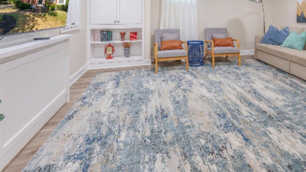Una sala de estar con un tapete estampado, dos sillones grises, un sofá beige y un mueble para televisión.