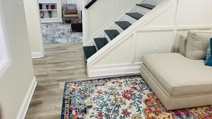 Una escalera con paredes blancas y peldaños negros que lleva a una habitación con un sofá color beige y un tapete colorido.