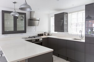 Una cocina moderna con armarios oscuros, encimera blanca, estufa a gas y una ventana con persianas.