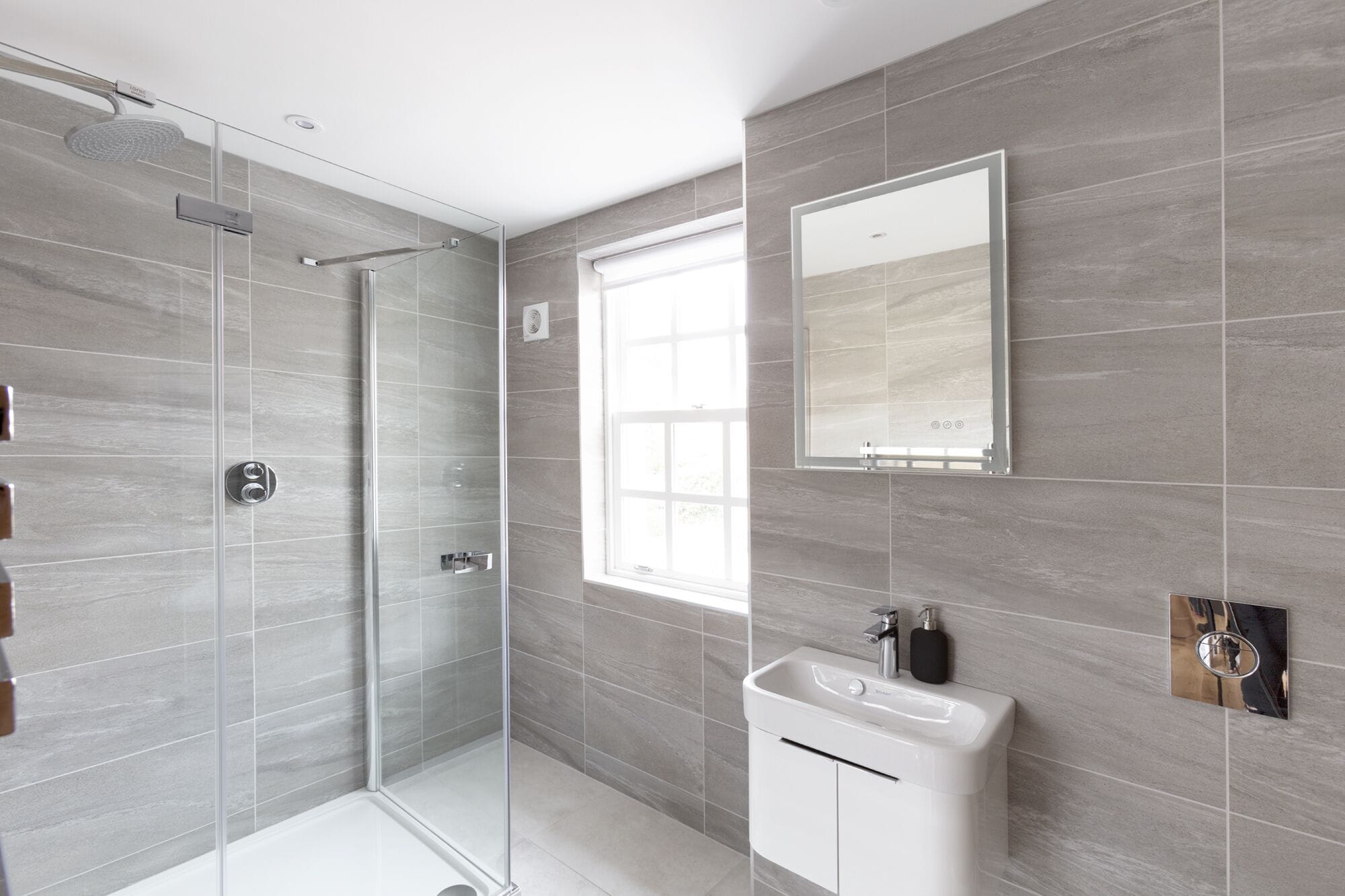 Une salle de bain moderne dotée d’une douche à parois de verre, d’un grand miroir et d’un lavabo avec un distributeur de savon.