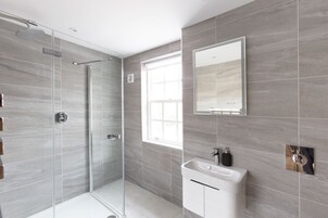Un baño moderno con cabina de ducha de vidrio, un espejo grande y un lavamanos con dispensador de jabón.