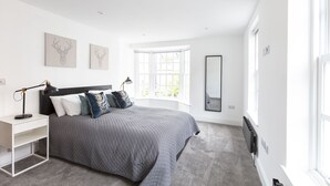 Un dormitorio moderno con cama, mesitas de noche, radiador y un ventanal grande.