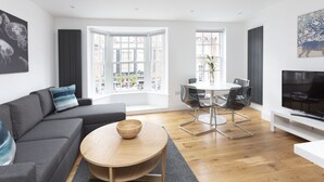 Una sala moderna con un sofá gris, una mesa de centro de madera y un comedor con mesa blanca y sillas negras.