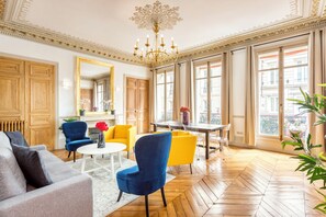 A spacious living room with a large window, wooden flooring, and a chandelier. - Merveil - Family Suite - Opera - Castellane (Paris)