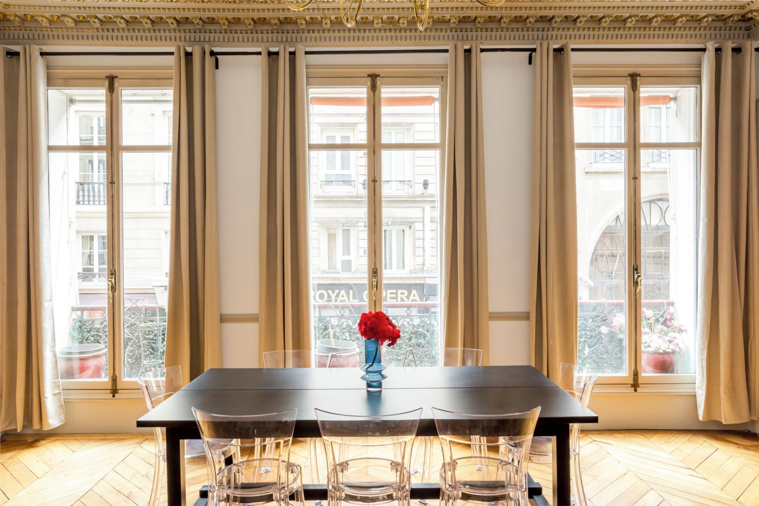 Un coin repas comprenant une table, des chaises et un vase avec une fleur rouge.