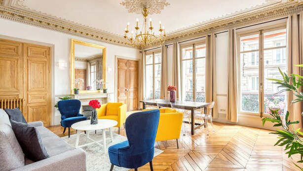 Ein geräumiges Wohnzimmer mit großem Fenster, Holzböden und einer Chandelüster.