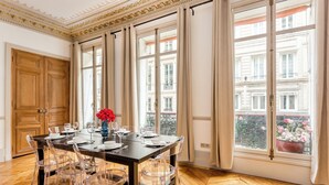 Ein Esszimmer mit einem großen Tisch, gedecktem für sechs Personen, transparenten Stühlen und einer Vase mit roten Blumen.