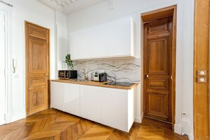 Une cuisine compacte avec des meubles blancs, un pare-feu en marbre et un plancher en bois disposé en chevrons.