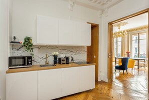 Eine moderne Küche mit weißen Schränken, einer Marmor-Spritzschutzwand und einer Holz Arbeitsplatte. Auf der Arbeitsplatte befinden sich ein Mikrowellenherd, ein Toaster und eine Pflanze.