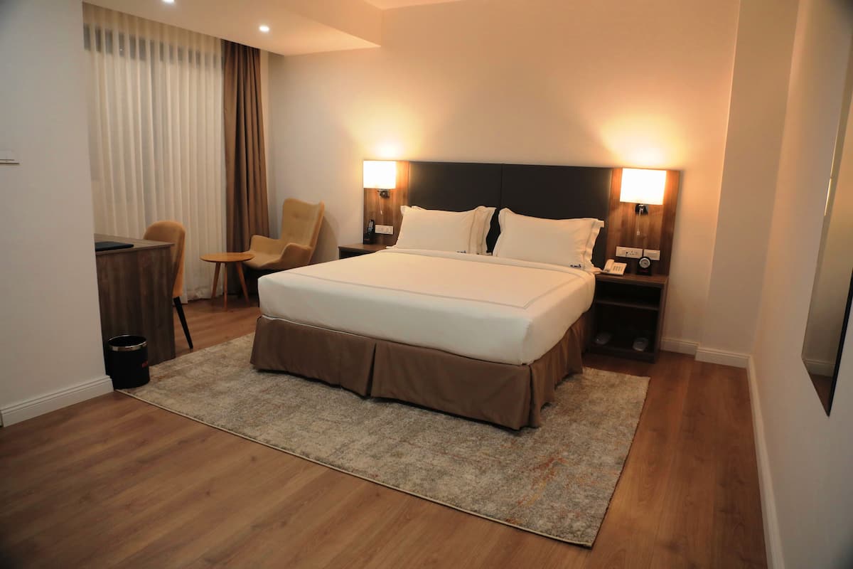 A hotel room with a large bed, two bedside tables, a chair, a desk, and a trash can.