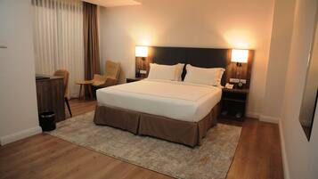 Habitación de hotel con una cama grande, dos mesitas de noche, una silla, un escritorio y un cubo de basura.