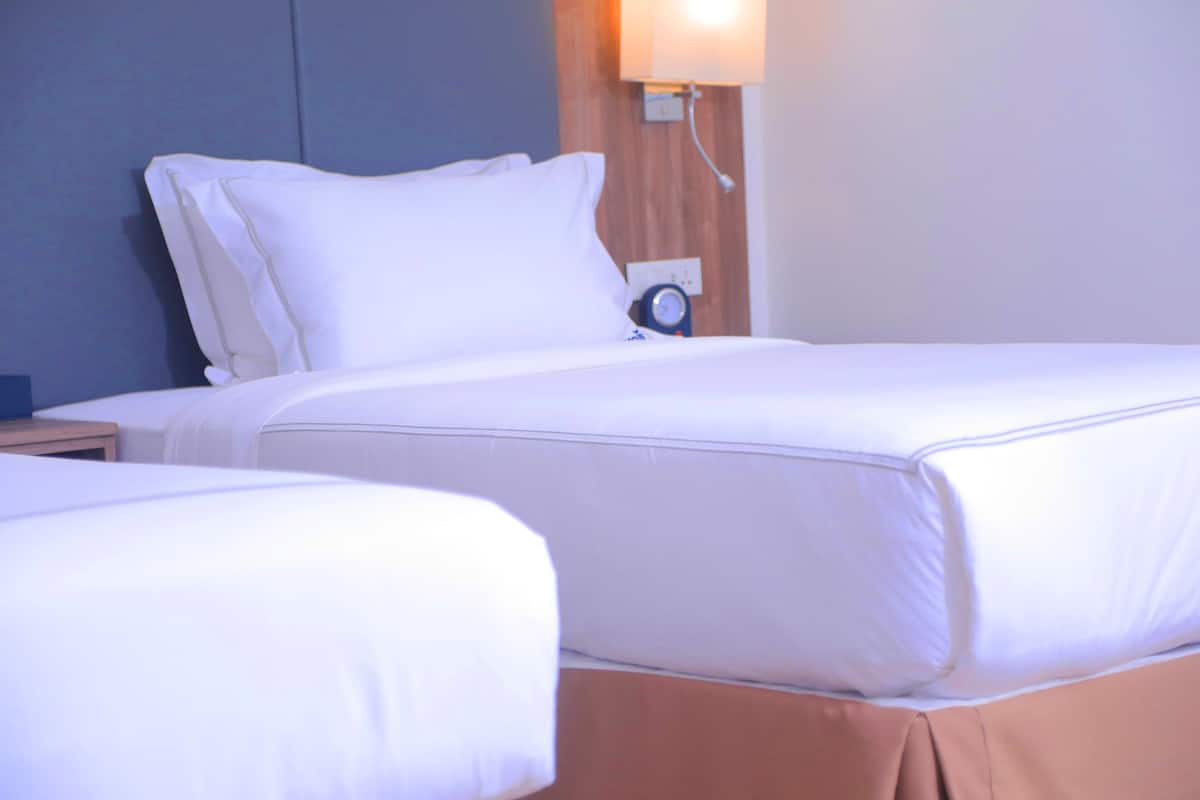 A hotel room with two beds, a nightstand, and a wall-mounted lamp.