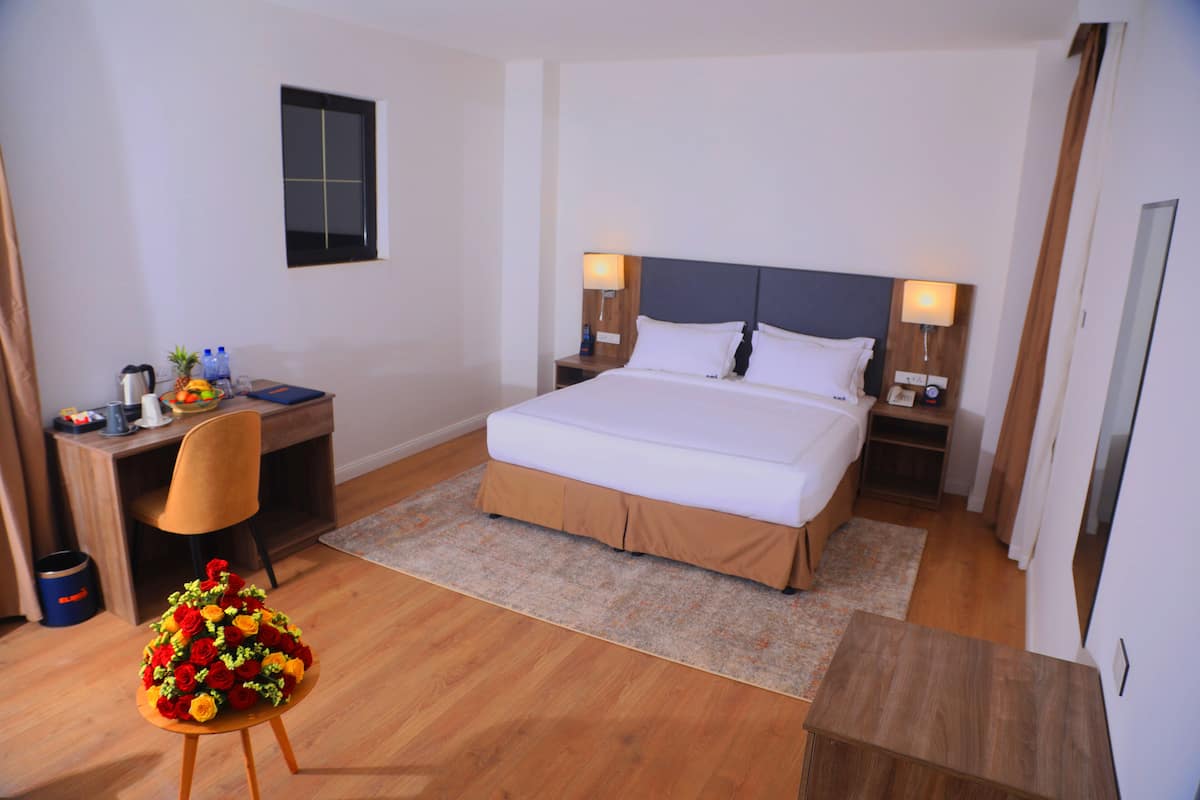 A hotel room with a bed, bedside tables, a desk, a chair, and a small table.