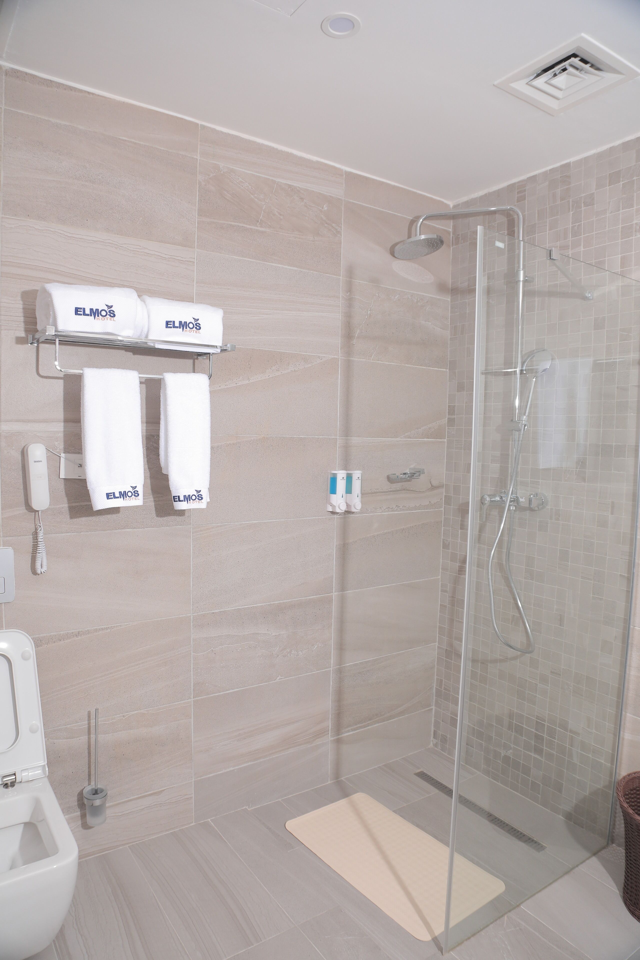 A modern bathroom with a glass-enclosed shower, a toilet, and a towel rack with two towels.