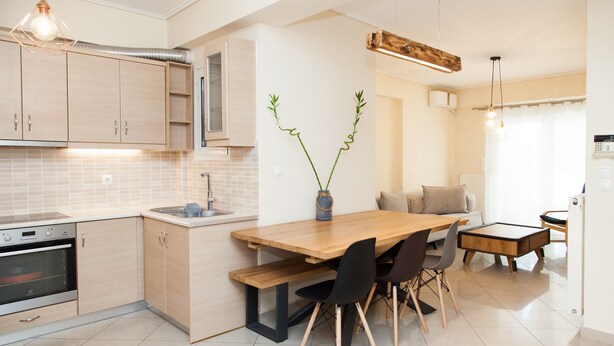 Una cocina moderna con armarios de madera clara, horno empotrado, mesa de madera con sillas y un jarrón con plantas verdes.