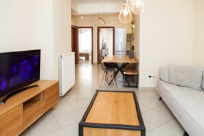 A modern living room with a flat-screen TV, a wooden coffee table, a sofa, and a dining area with a table and chairs. - Amazing Apt in Tauros (Moschato-Tavros)