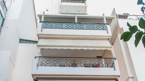Un edificio de varios pisos con balcones, fachada de piedra y un coche estacionado en la entrada.