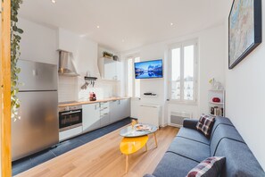 A modern apartment with a kitchen, dining area, and living room. It features a large TV, a sofa, and a coffee table.