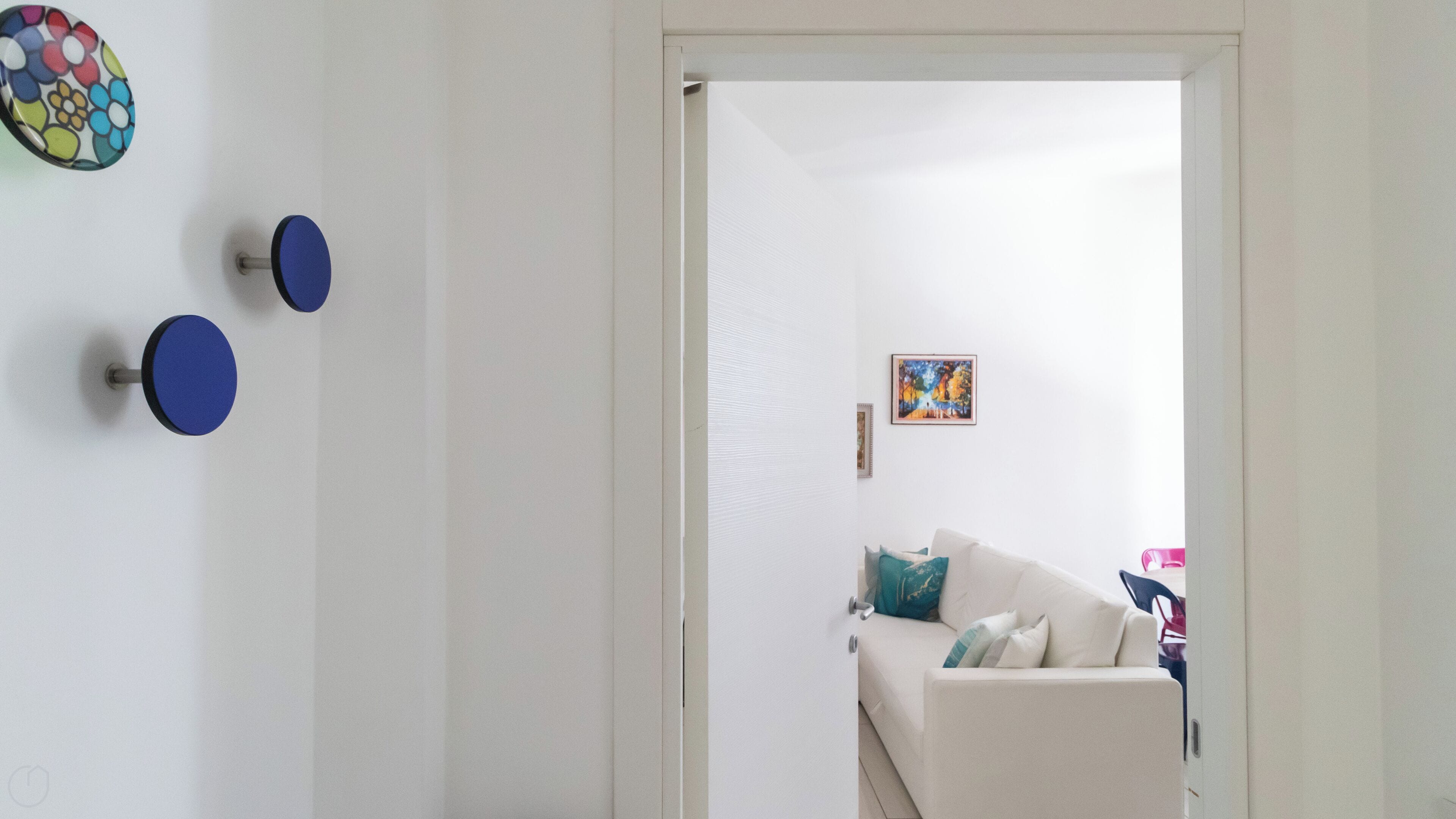 A white room with a white sofa, a door leading to another room, and three blue circular wall decorations.